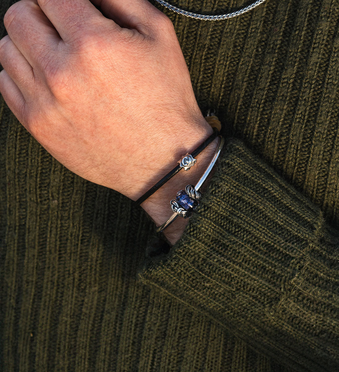 Trollbeads Sunshine silver bead on a leather bracelet complemented by a silver bangle with a blue glass bead and two silver spacers on a male model wearing a green knit sweater